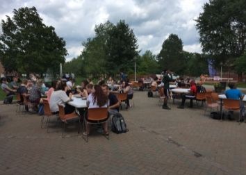 Students sitting at picnic tables with trees behind them.