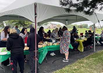 People outdoors under a tent assembling plates of food to eat for a gathering.