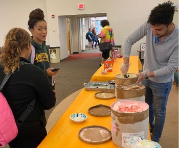 A person scoops ice cream from a container at a table while two others wait to be served.