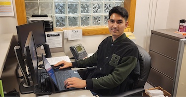 A JCC campus student worker sits a desk with a computer.