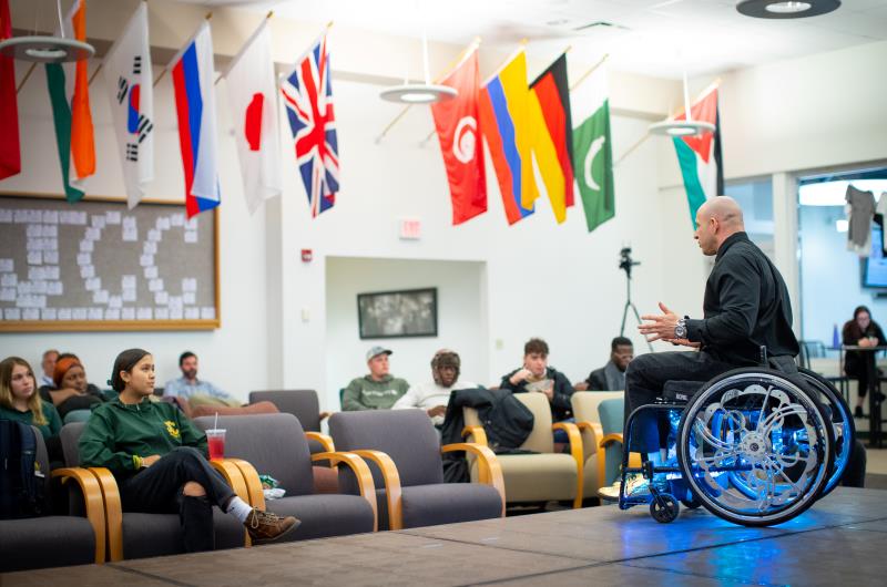 A person sitting in a wheelchair speaks to an audience of students.