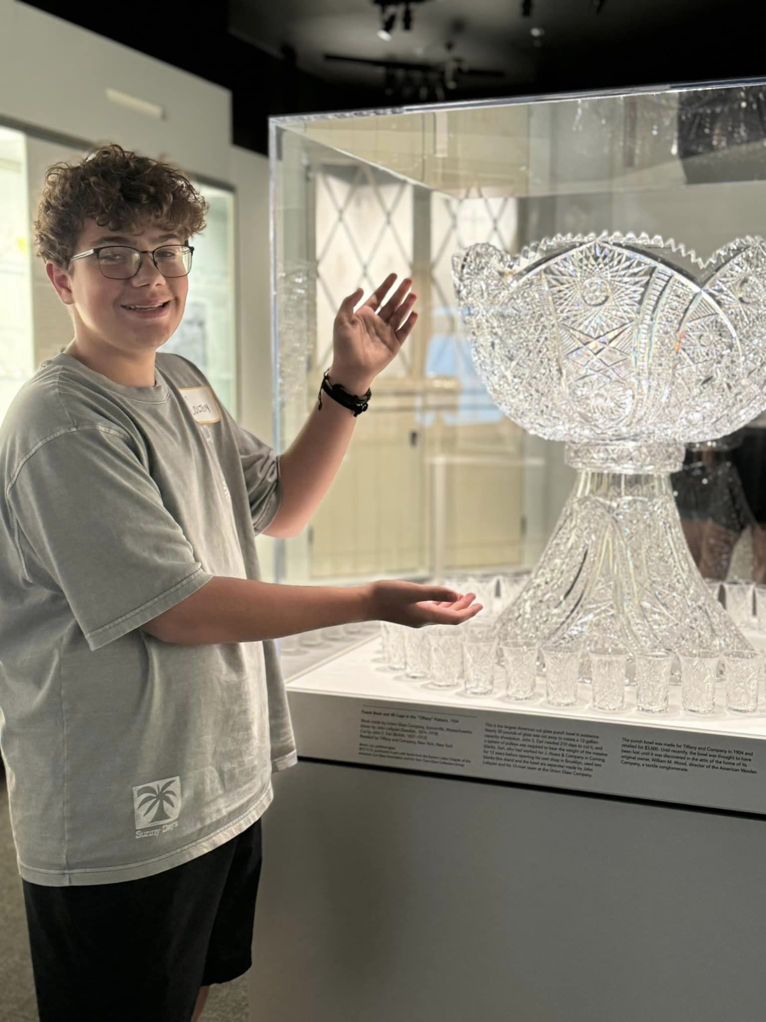 A smiling student holds out their arms to showcase a display of beautiful glass.