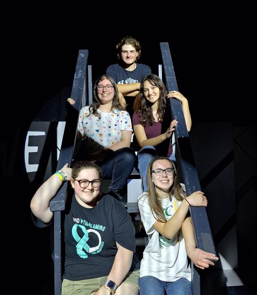 A cast of five student actors posing on a staircase.