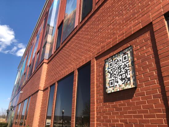 A look at a QR code made of tile on the side of a building with a mural.