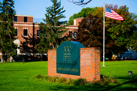 The brick with arching dark green sign emblazoned with the gold letters that say SUNY JCC that greets students and visitors at the North County Extension Center in Dunkirk, NY.