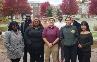 Students stand together on the SUNY Jamestown Community College Jamestown Campus, with snow beginning to cover the grass and trees still holding their fall leaves.