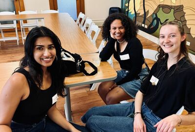 Three JCC international students smile while sitting together at a table.