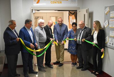 Eight people smile while they hold yellow and green ribbons that are being cut to open the YMCA JCC Early Learning Center.